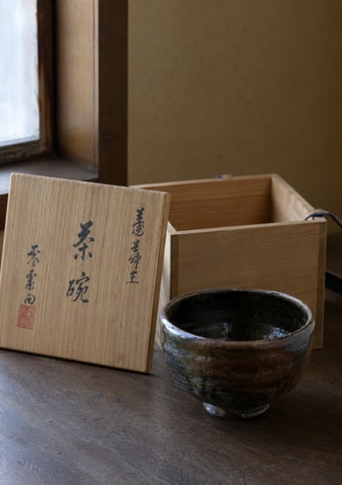 Handmade ceramic Japanese chawan tea bowl next to its traditional wooden storage box.