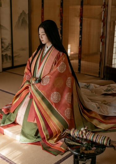 A woman wearing a traditional Japanese junihitoe multi-layered silk kimono sitting on a tatami floor.