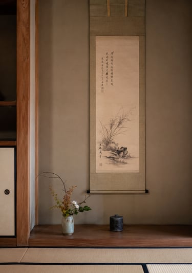 Minimalist Japanese tokonoma with a hanging scroll, ikebana floral arrangement, and tatami flooring.