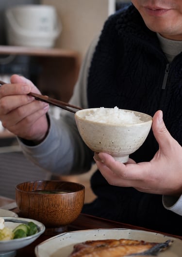A person eating a traditional Japanese breakfast with white rice, miso soup, and grilled fish.