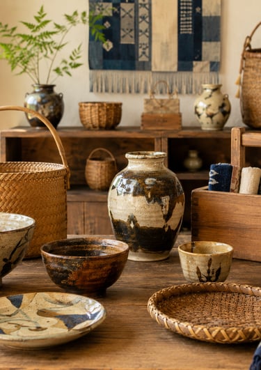 Rustic Japanese pottery, woven bamboo baskets, and kokeshi dolls on a wooden table.