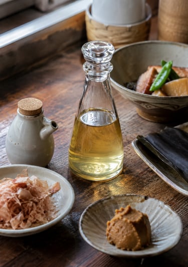 Traditional Japanese cooking ingredients including dashi stock, miso paste, and dried bonito flakes on a rustic table.