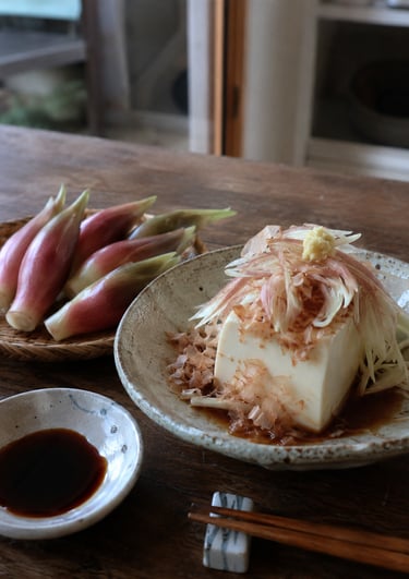 Hiyayakko Japanese cold tofu topped with bonito flakes and sliced myoga ginger on a wooden table.