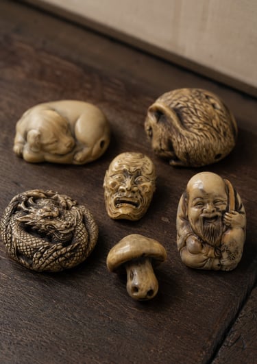 Collection of antique Japanese netsuke carvings featuring a dragon, mask, and figures on wood.