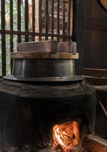 Traditional Japanese wood-fired clay stove cooking rice in a metal pot with a wooden lid.