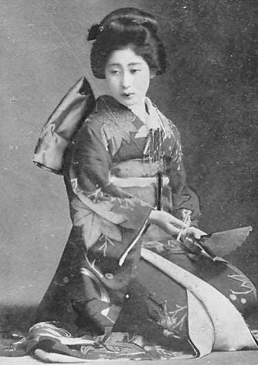 Vintage portrait of a Japanese woman in a traditional floral kimono and obi, holding a folding fan.