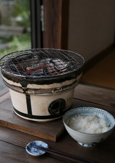 Traditional Japanese shichirin charcoal grill with a bowl of white rice on a wooden table.