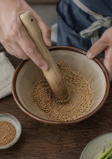 Chef using a wooden pestle to grind toasted sesame seeds in a ceramic Japanese suribachi mortar bowl.