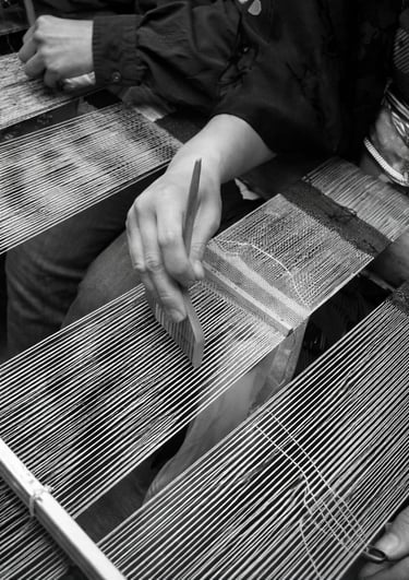 Close-up of a weaver using a traditional wooden comb tool on a handloom for intricate textile weaving.