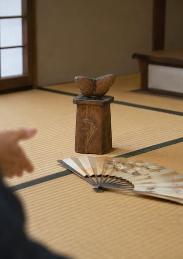 A wooden butterfly sculpture and folding fan on a traditional Japanese tatami floor.