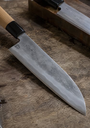 Hand-forged Japanese Santoku kitchen knife with carbon steel blade on a wooden cutting board.