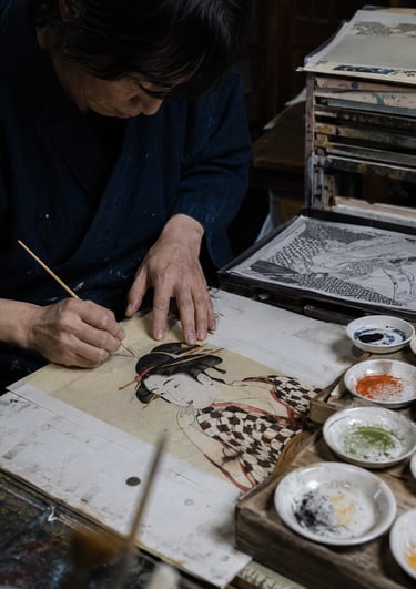 A Japanese artist hand-painting a traditional Ukiyo-e woodblock print portrait of a woman.