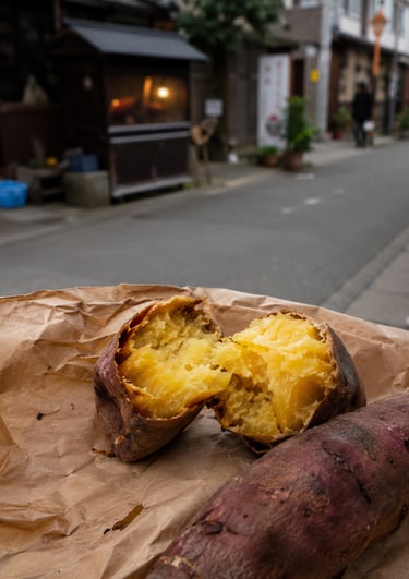 Roasted Japanese sweet potato split open on brown paper with a blurred Tokyo street background.