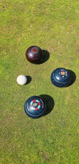 Three porthcawl bowls club bowls on grass near a white jack