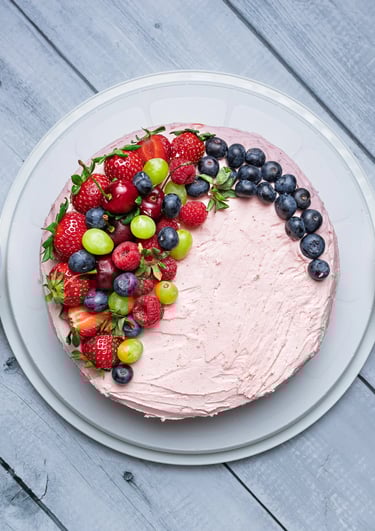 a cake with fruit on a table with bowls of fruit