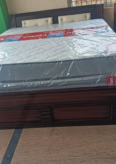 Modern dark wood double bed frame with a white quilted mattress wrapped in protective plastic.