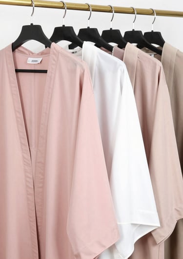 Soft pastel abayas draped elegantly on wooden hangers against a minimalist white backdrop.
