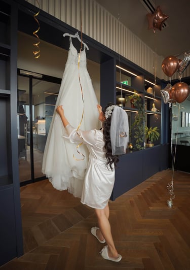 Bride in a silk robe reaching for her wedding dress before the ceremony, captured by Fred Art Studio