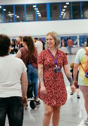 A woman in a red dress with a volunteer badge smiles at event goers