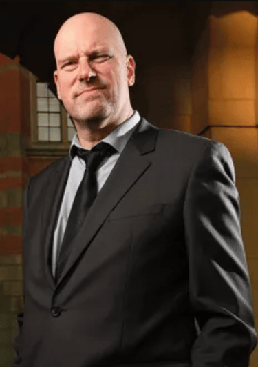David Gillborn in a suit and tie standing in front of a building