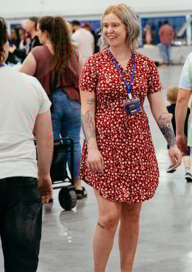 A woman in a red dress with a volunteer badge smiles at event goers
