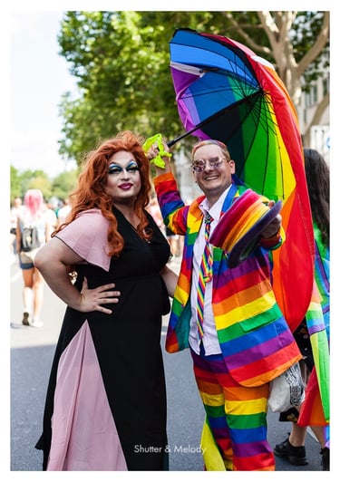 Eine Drag Queen und ein Mann mit Regenbogenanzug, Hut und Regenschirm bei der Christopher Street Day