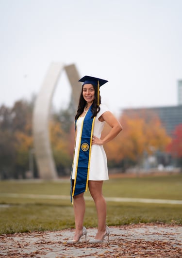 Graduation portrait at UC Merced featuring a senior in a white dress and cap in front of the statue