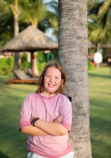 Individual portrait of a boy smiling by a palm tree during a family photoshoot at Mövenpick Resort P