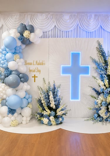 Elegant blue and white baptism backdrop featuring a glowing cross, balloon arch, and floral arrangements.