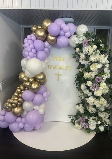 Elegant lavender, gold, and white balloon arch with floral garland for a first communion celebration.