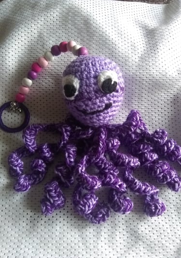 Pulpo de peluche morado hecho a mano a crochet con tentáculos rizados y un clip rosa con cuentas.
