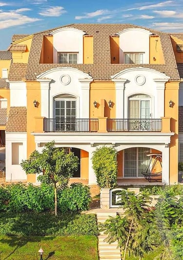 Luxurious yellow Mediterranean villa with white arches, balconies, and lush green landscaping.