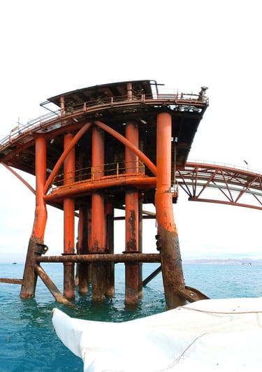 An offshore oil rig platform with weathered orange pillars standing in blue ocean water.