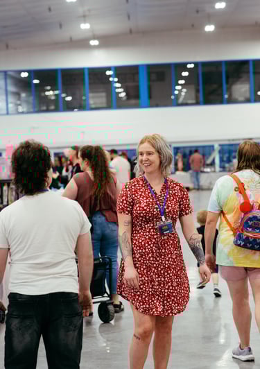 A woman in a red dress with a volunteer badge smiles at event goers