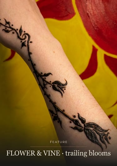 Intricate black henna tattoo featuring a delicate flower and vine design on a person's forearm.