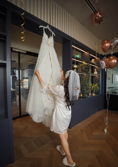 Bride in a silk robe reaching for her wedding dress before the ceremony, captured by Fred Art Studio