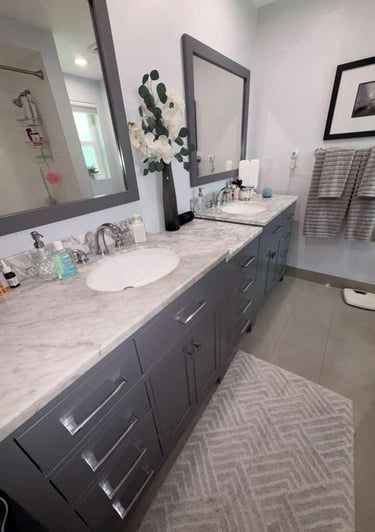 Modern bathroom with double vanity, grey cabinets, white marble countertops, and large mirrors.
