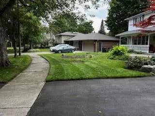 A quiet suburban street with a mowed green lawn, paved driveway, and modern single-family houses.
