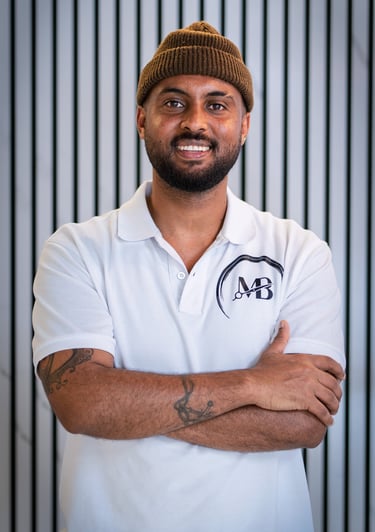well lit Portrait photo of Maji, Co-owner of MB Barbers Manchester, posing with a smile and his arms crossed