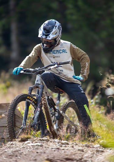 Mountain biker in a full-face helmet and jersey resting on a forest trail with his downhill bike.