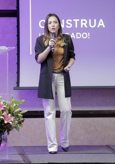 uma mulher em pé encima de um palco, em frente a um projetor de imagens com um microfone