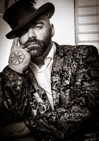 black & white portrait of man in top hat with feather looking seductively wearing shiny blazer