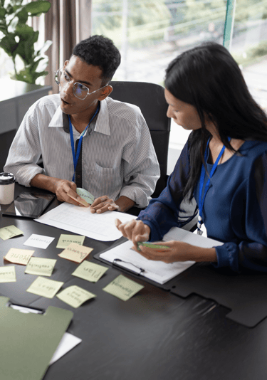 a man and woman sitting at a table with sticky notes