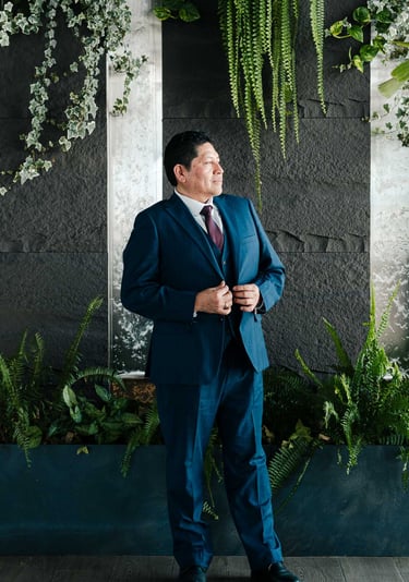 Retrato corporativo profesional y elegante de hombre en traje azul en un fondo con plantas verdes en Quito Ecuador