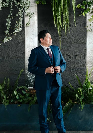 Retrato corporativo profesional y elegante de hombre en traje azul en un fondo con plantas verdes en Quito Ecuador
