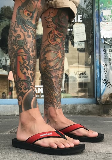 seorang pria dengan tato di kakinya menggunakan sandal gunung Sabertooth