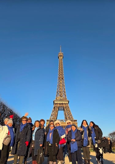 Un grupo de turistas con bufandas azules posan frente a la Torre Eiffel bajo un cielo azul despejado en París.
