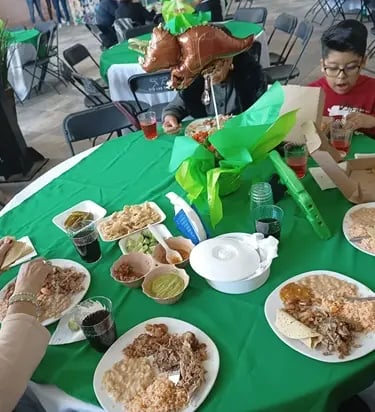 Familia disfrutando barbacoa con arroz y frijoles en una mesa verde durante una fiesta infantil.