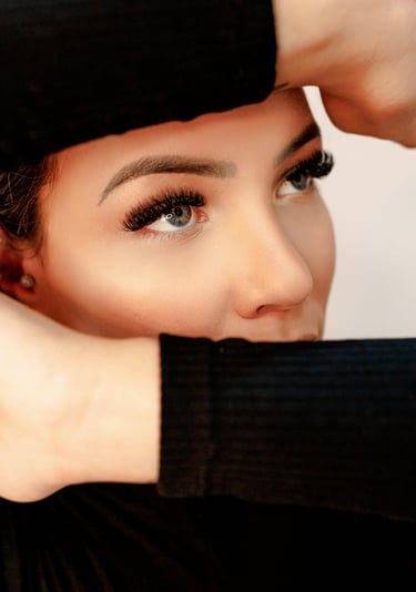 Primer plano de una mujer con extensiones de pestañas largas y cejas delineadas posando con sus mano