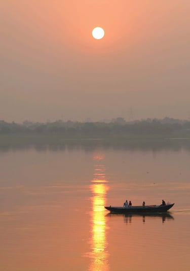 Silhouetted traditional boat carrying people on the Ganges River during a golden sunrise in Varanasi.